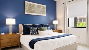 A bedroom with a bed, two bedside tables, a nightstand, a window with curtains, and a wall-mounted artwork. - Marco Island Escape Pool Game Room (Marco Island)