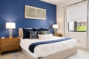 A bedroom with a bed, two bedside tables, a nightstand, a window with curtains, and a wall-mounted artwork. - Marco Island Escape Pool Game Room (Marco Island)
