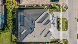 A multi-level building with a geometric roof design, surrounded by a landscaped area with palm trees. - Marco Island Escape Pool Game Room (Marco Island)