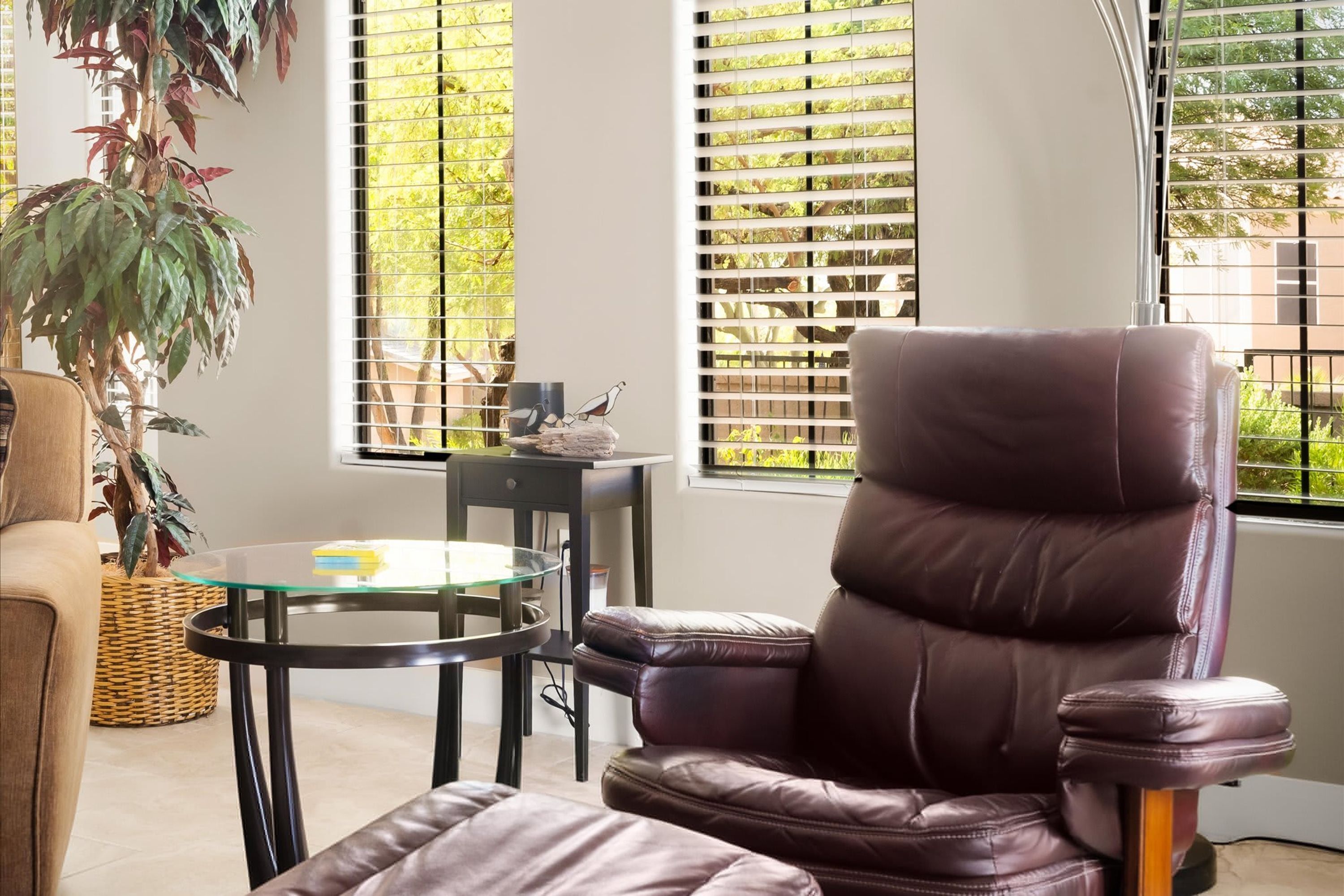 A room with a leather chair, a glass table, a wicker basket, and a potted plant.