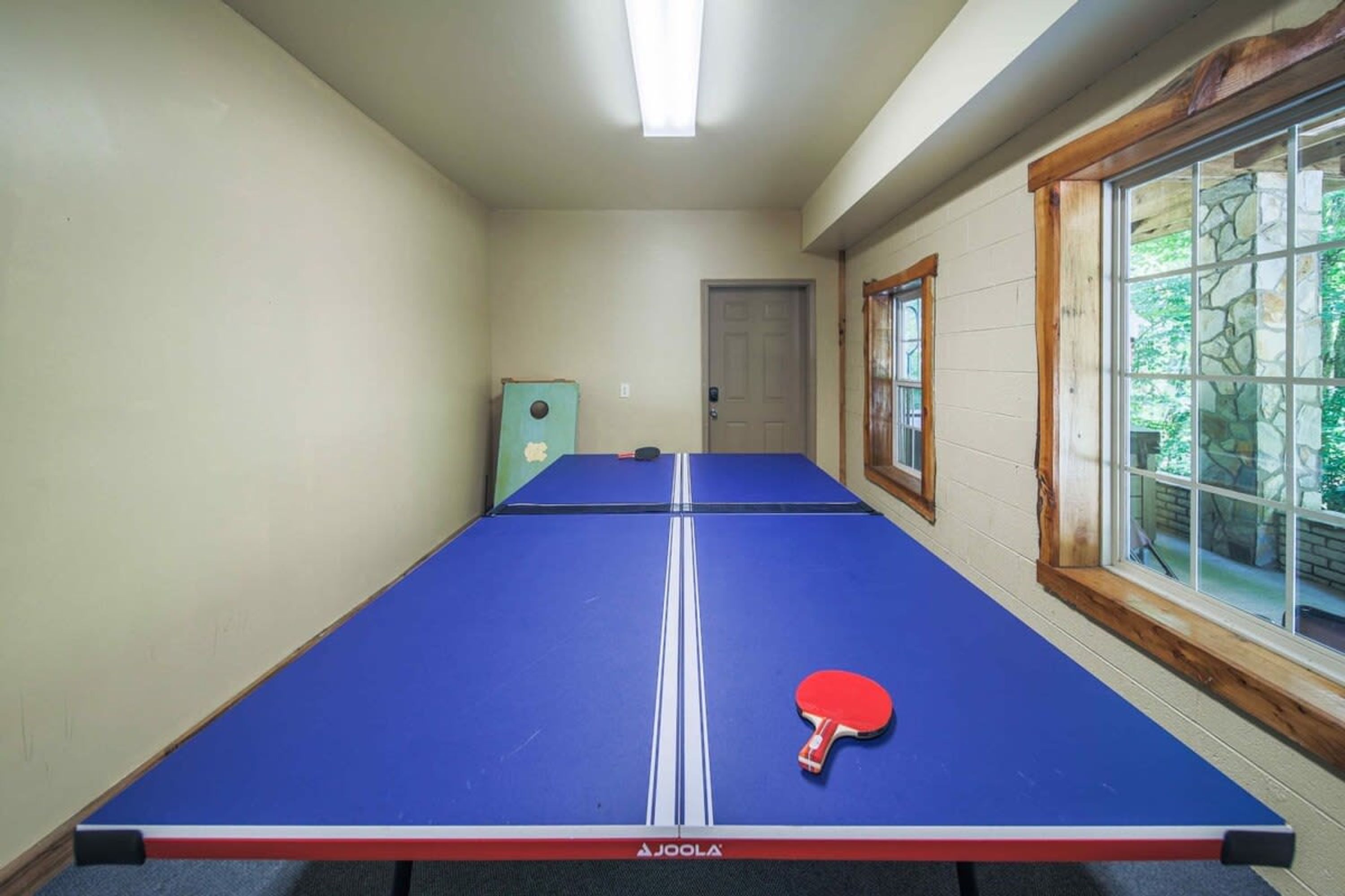 Una mesa de ping pong con una paleta en una habitación con puerta y ventanas.