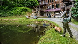 A person fishing by a pond with a dog, a wooden building in the background, and a clear sky. - Sleeps 16 Hot Tub Sauna Dogs Welcome Ping Pong (Mars Hill)