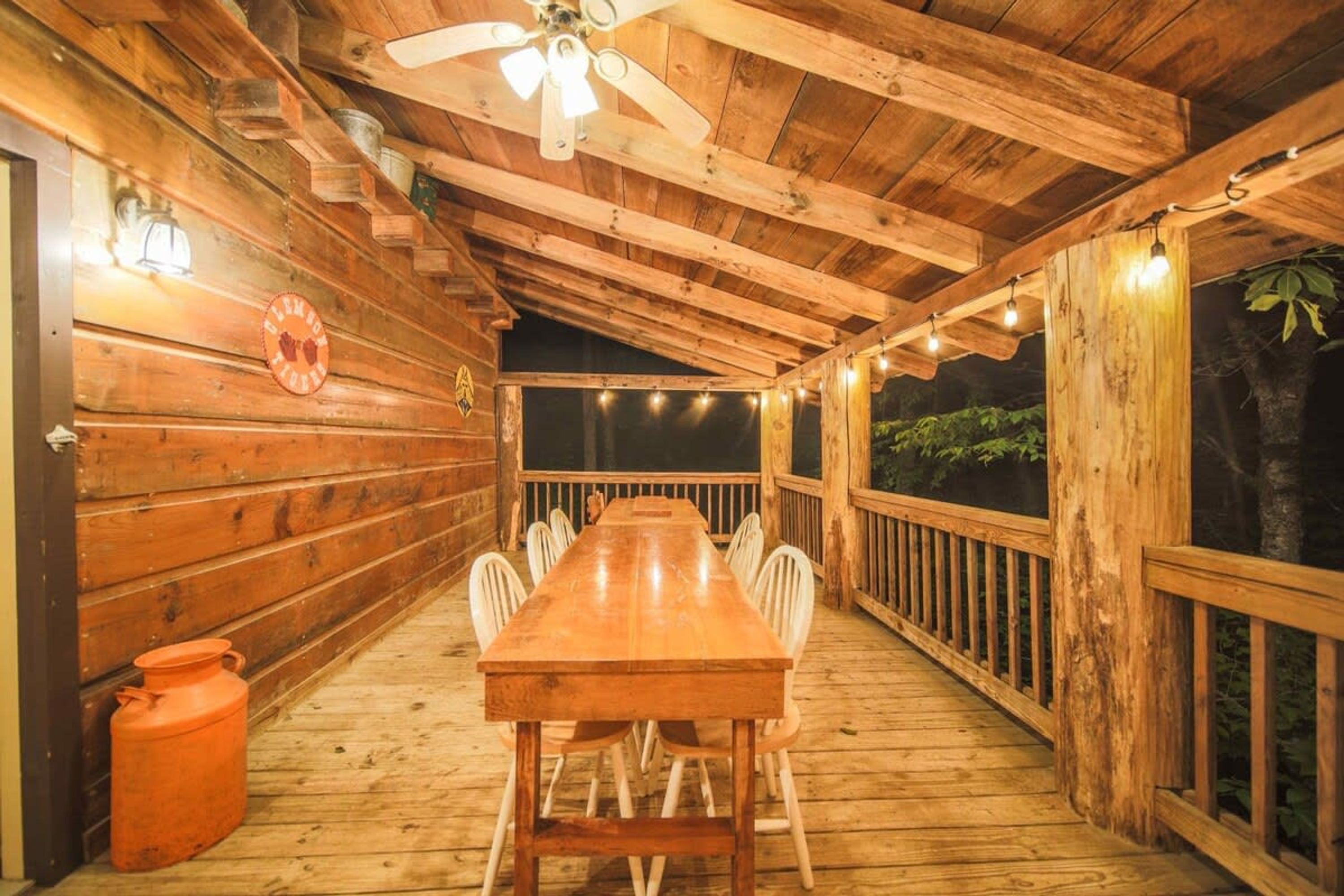 A wooden deck with a long table and chairs, a ceiling fan, and string lights.