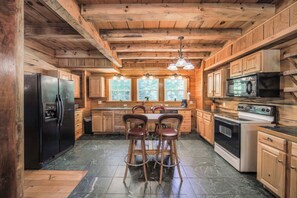 A wooden cabin-style kitchen with a central island, bar stools, and a refrigerator. - Sleeps 16 Hot Tub Sauna Dogs Welcome Ping Pong (Mars Hill)