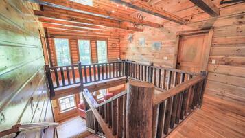 A wooden cabin interior with a balcony, wooden walls, and a door.