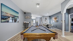 A pool table in a room with a view of a landscape painting, a welcome sign, and a dining area with chairs. - Heated Pool Game Room Outdoor Fun Sleeps 6 (Tampa)