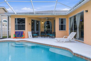 Ein Swimmingpool mit überdachtem Patio, inklusive Liegestühlen und Deckenventilator.
