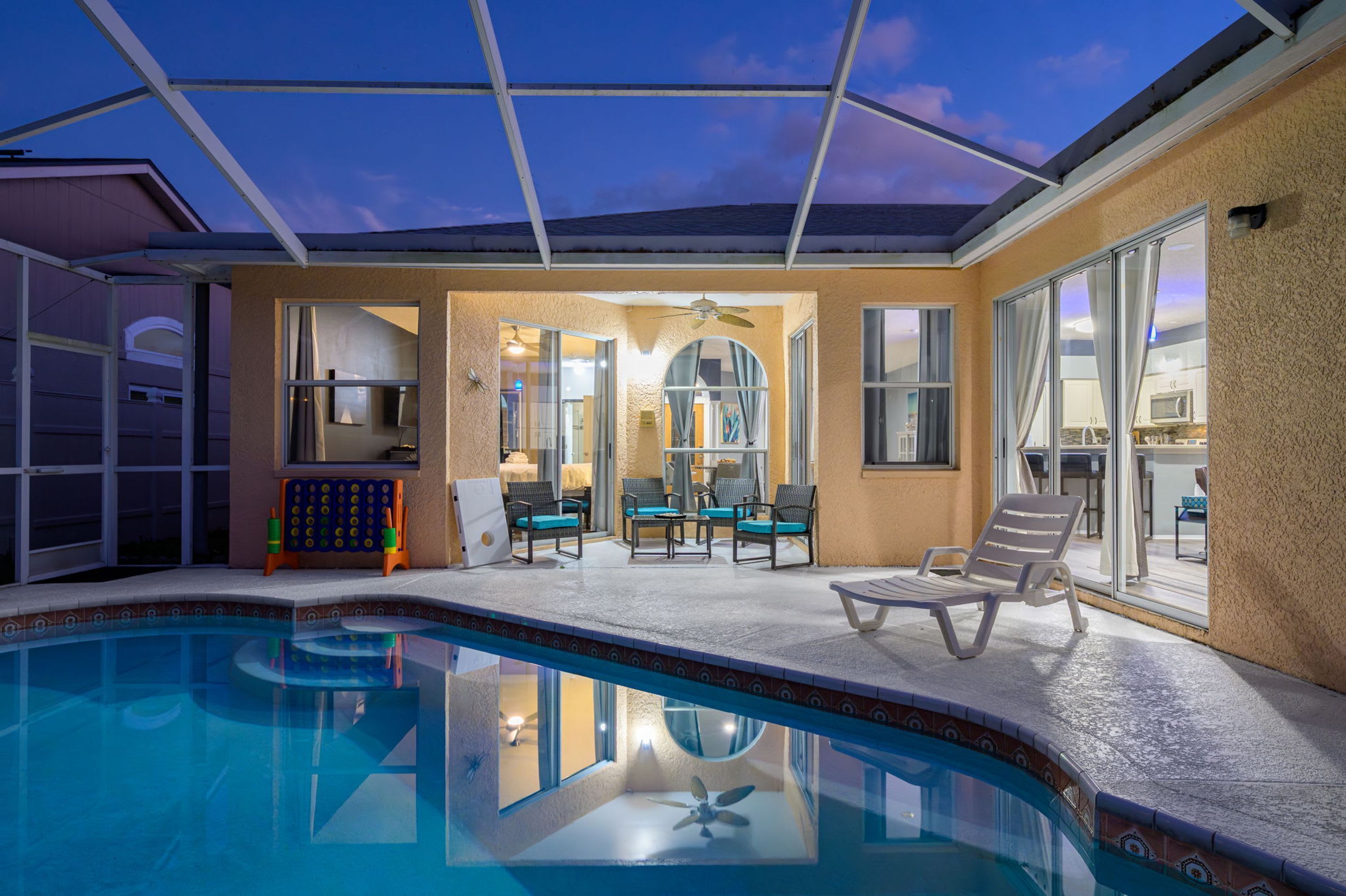 A pool area with a covered patio, chairs, and a view of the interior.