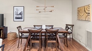 Un coin repas avec une table et des chaises en bois, un luminaire suspendu, un tableau encadré au mur et un radiateur.