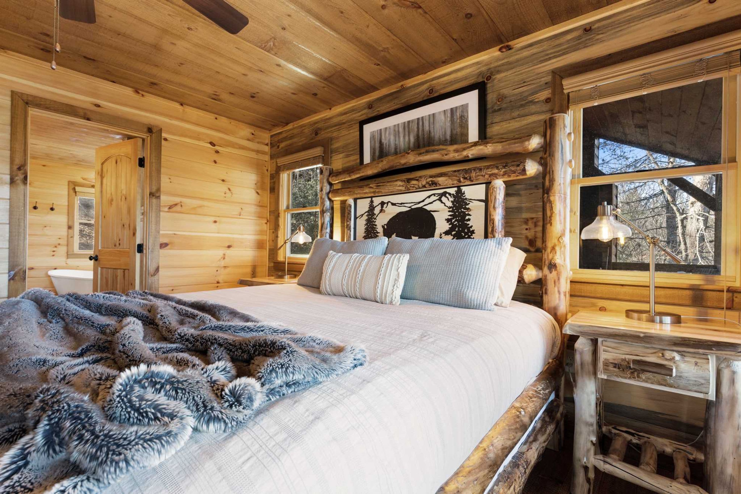 A wooden cabin bedroom with a bed, a wooden headboard, a window, and a bedside table.
