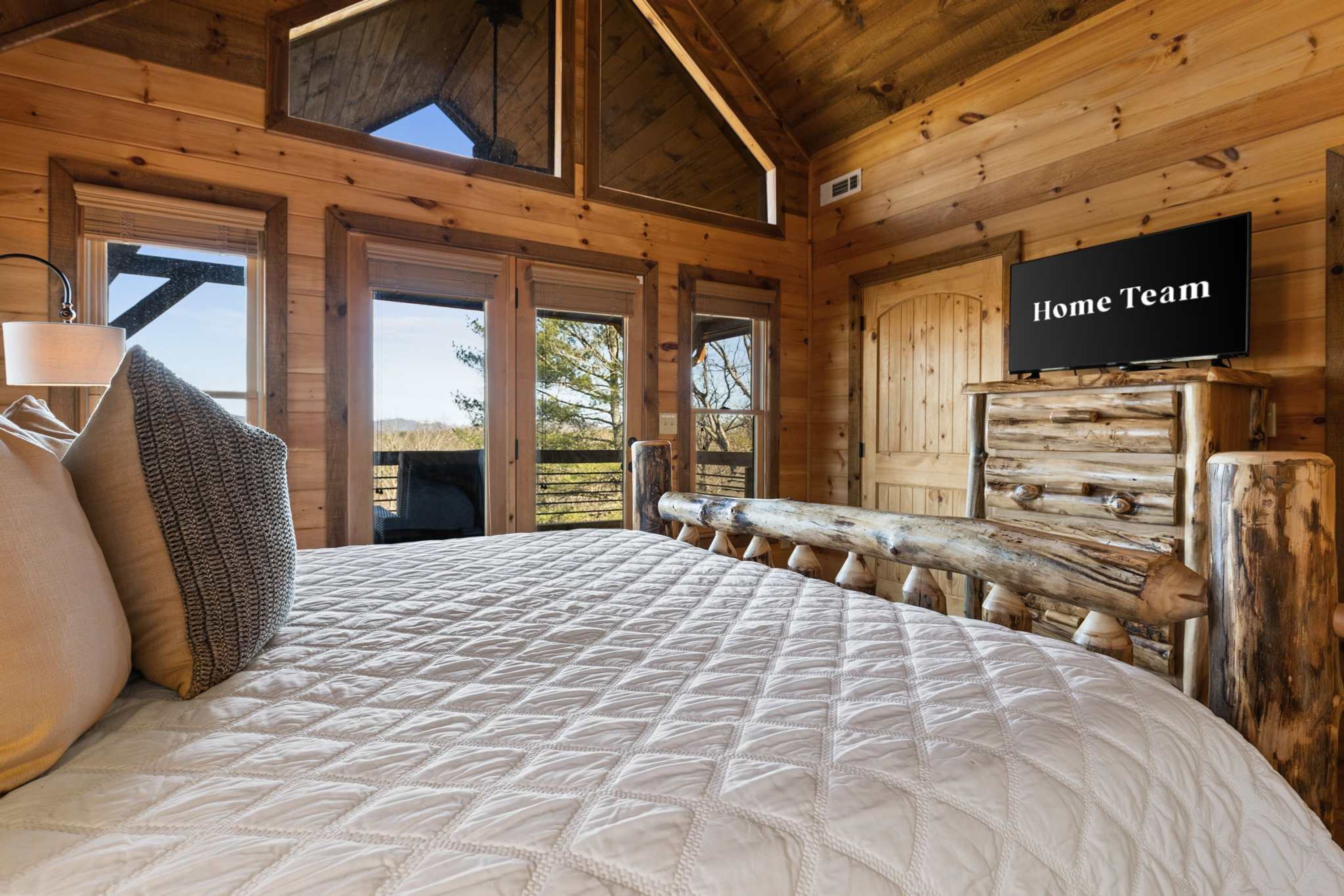 A bedroom with a large bed, a television, and a view of the outdoors.