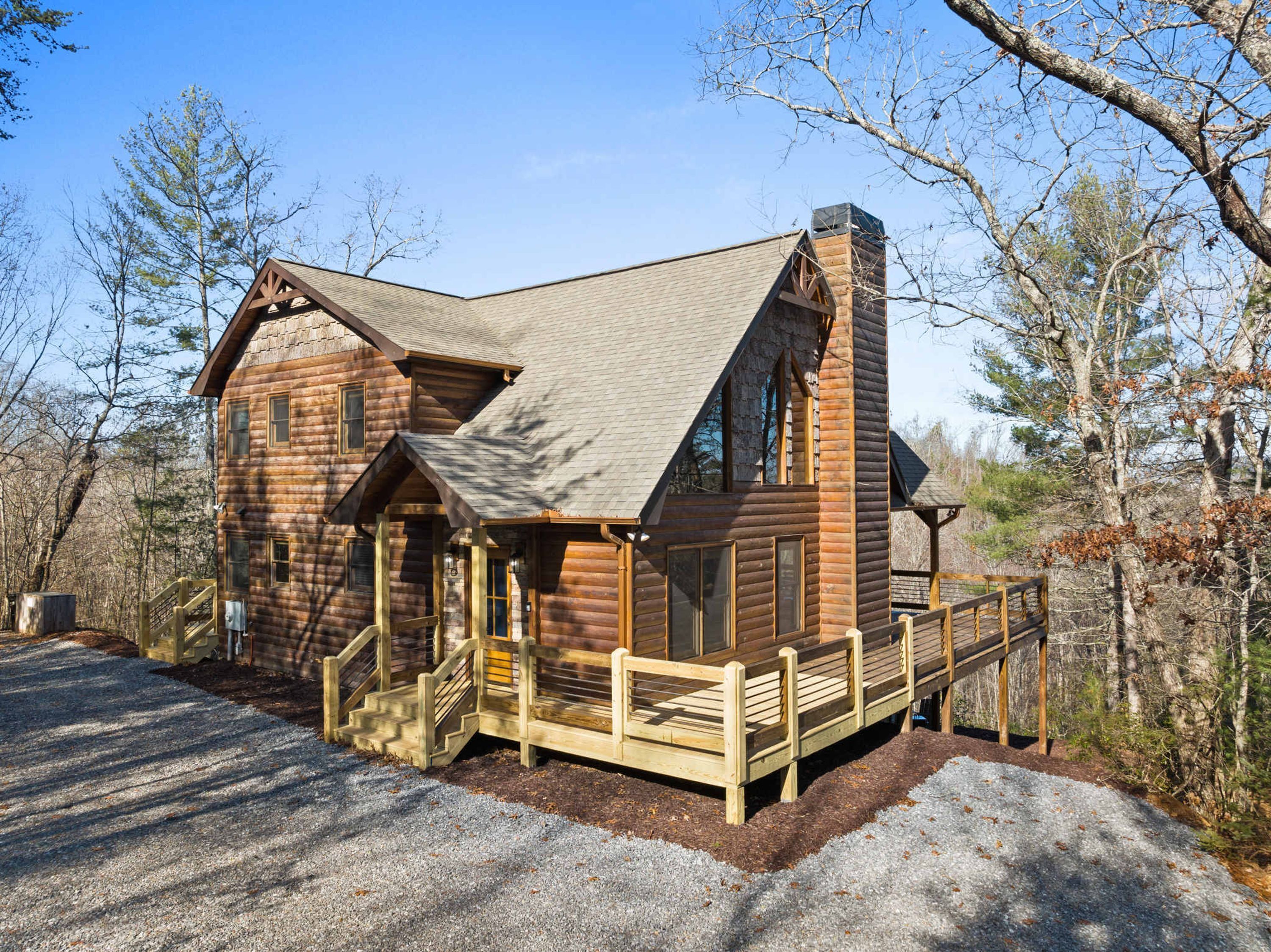 A log cabin with a steeply pitched roof, a chimney, and a wooden porch with steps leading to a bench.