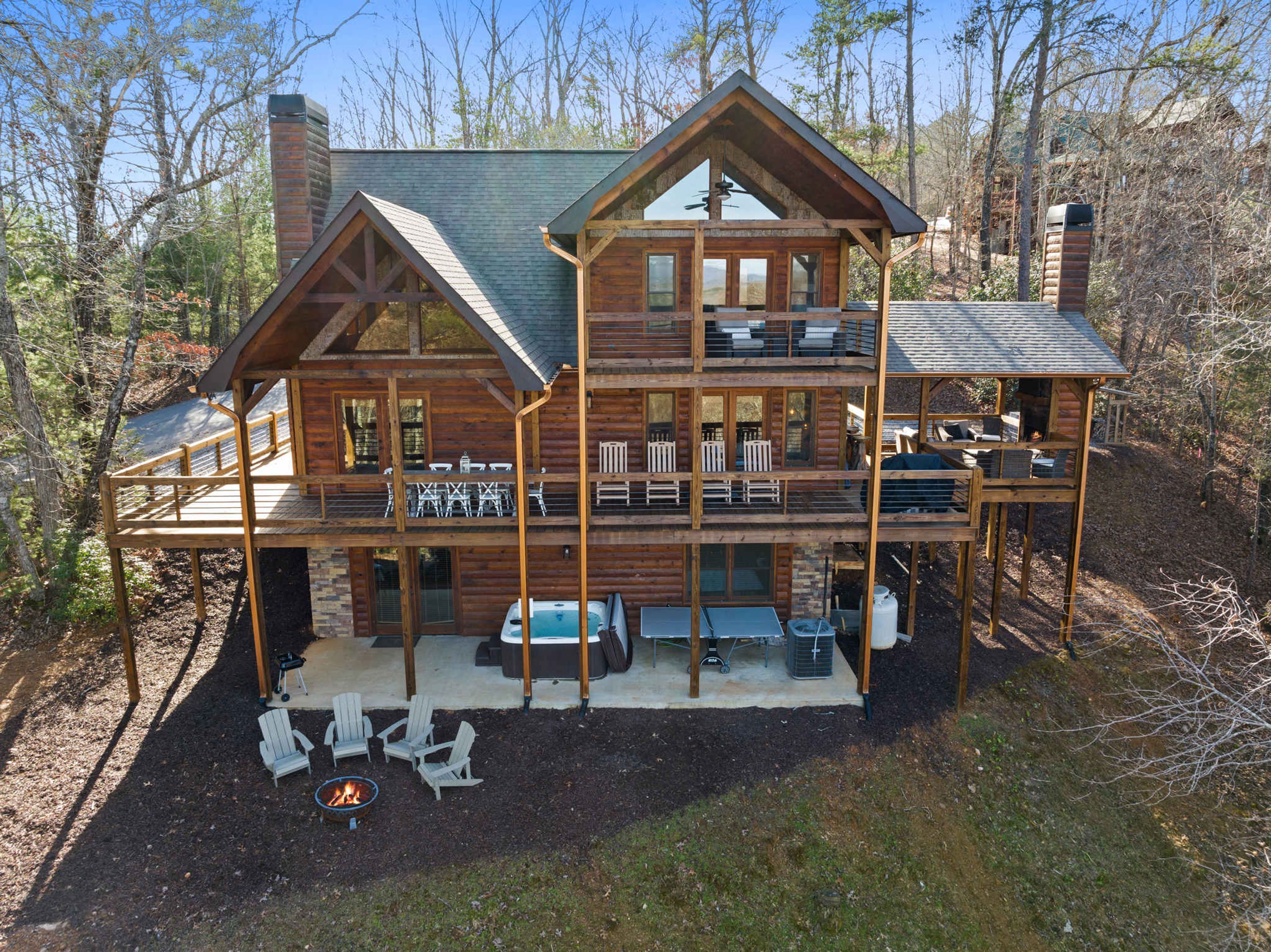 A multi-level log cabin with outdoor seating, a fire pit, and a deck.