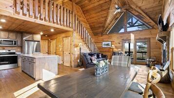 A spacious wooden cabin interior with a kitchen, dining area, and a loft bedroom.