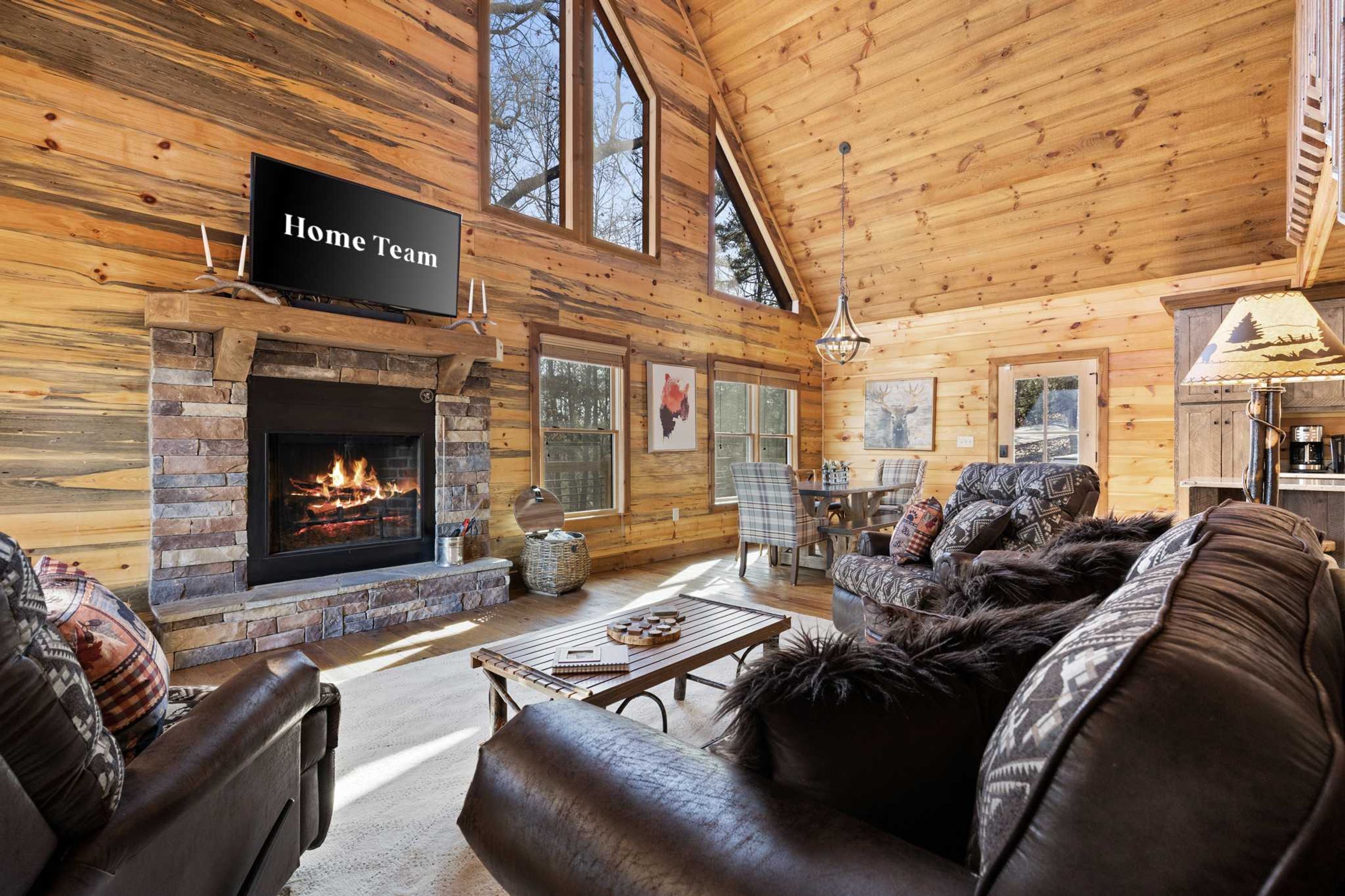 A log cabin interior with a fireplace, a television labeled 'Home Team,' and a cozy seating area.