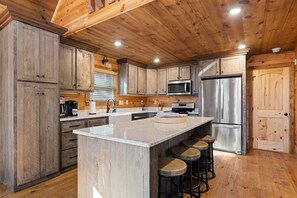 Una cocina con gabinetes de madera, un refrigerador de acero inoxidable, un microondas y una isla grande con taburetes.
