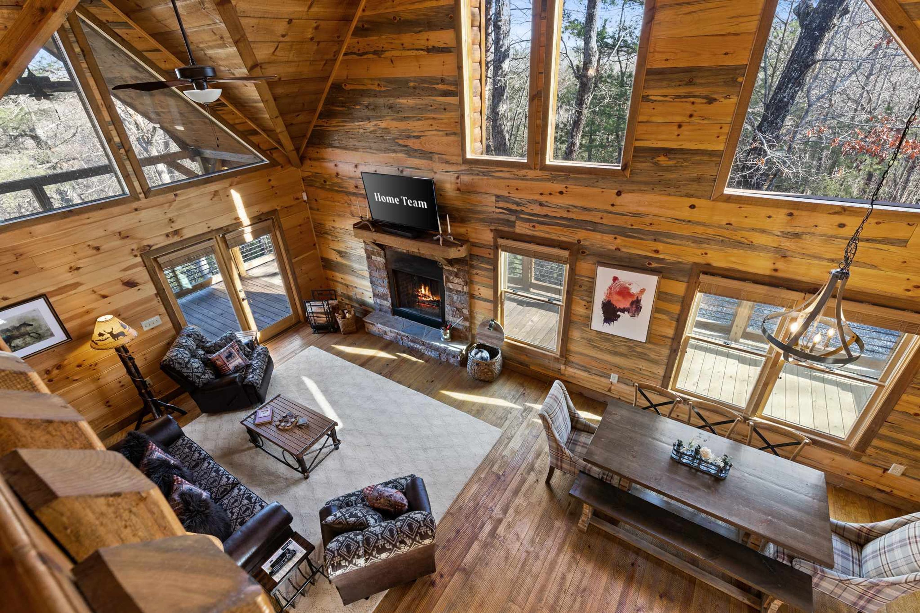 A log cabin interior with a fireplace, seating area, and large windows.