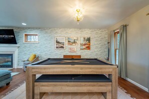 Ein Zimmer mit Billardtisch, Kamin und gerahmten Kunstwerken an der Wand.