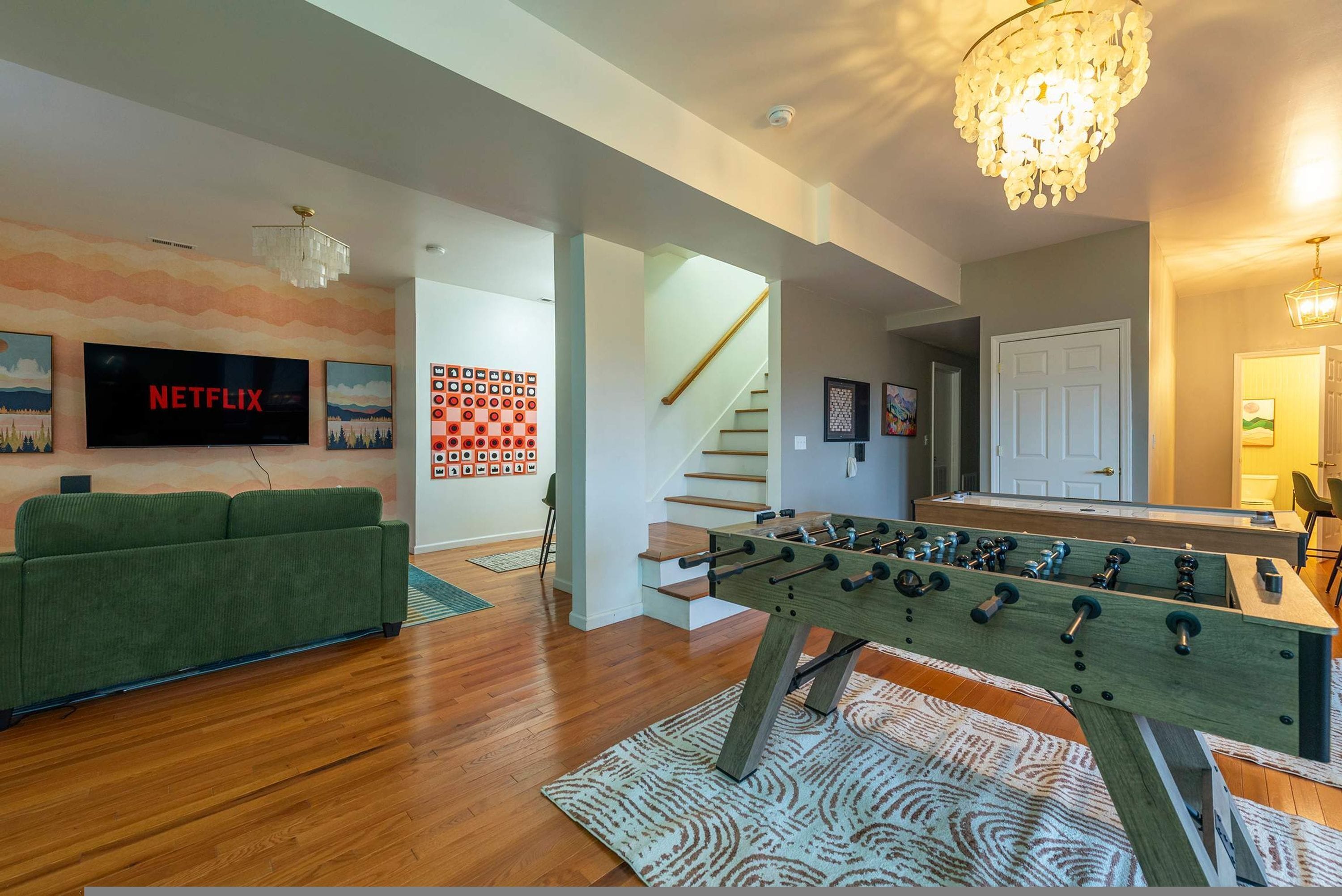 A living room with a foosball table, a green sofa, a flat-screen TV, and a staircase.