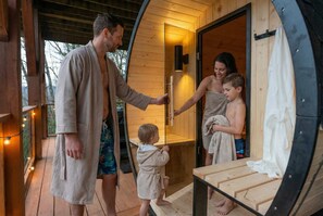 Una familia entrando a una sauna de madera con un banco y una puerta.