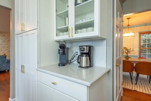 Une cuisine avec des meubles blancs, une machine à café et une cafetière.