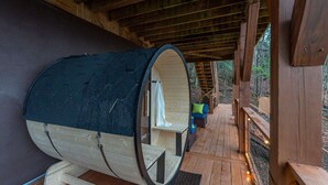 En træhytte med sauna, træterrasse og udsigt til skoven.