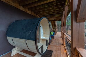 Eine Holz-Blockhütte mit Sauna, einer Holzdiele und Blick auf den Wald.