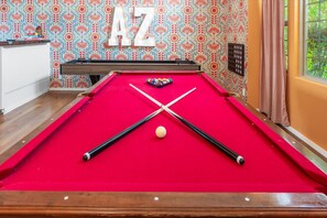 A pool table with a red felt surface, two pool cues, and a cue ball. - Pickleball Heated Pool Spa Sleeps 16 (Peoria)