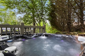 Ein Whirlpool mit Holzterrasse und Wasserfall, umgeben von Bäumen.