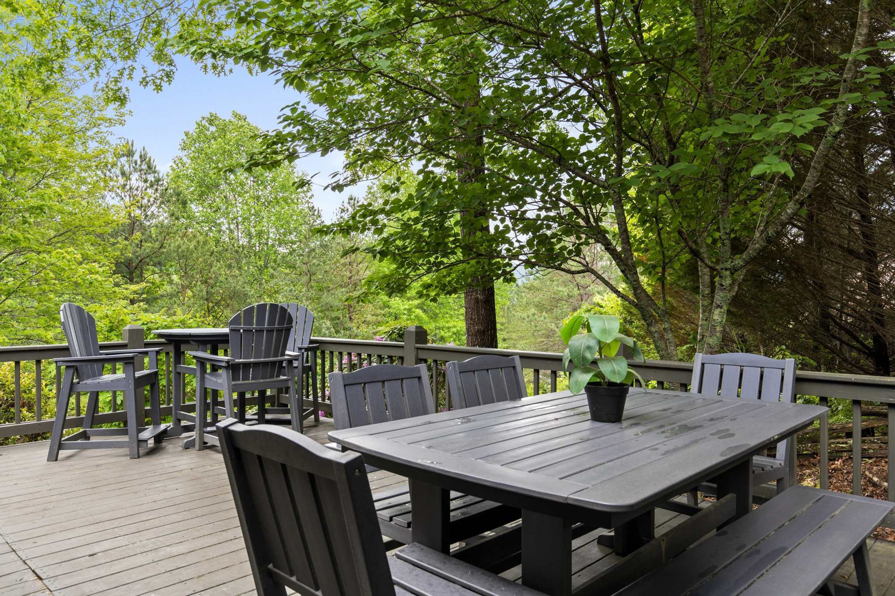 An outdoor deck with a wooden table and chairs, surrounded by trees.