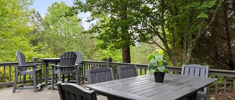 An outdoor deck with a wooden table and chairs, surrounded by trees.