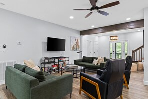 Ein modernes Wohnzimmer mit Flachbildfernseher, grünen Sofas, einem Couchtisch und Deckenventilator.
