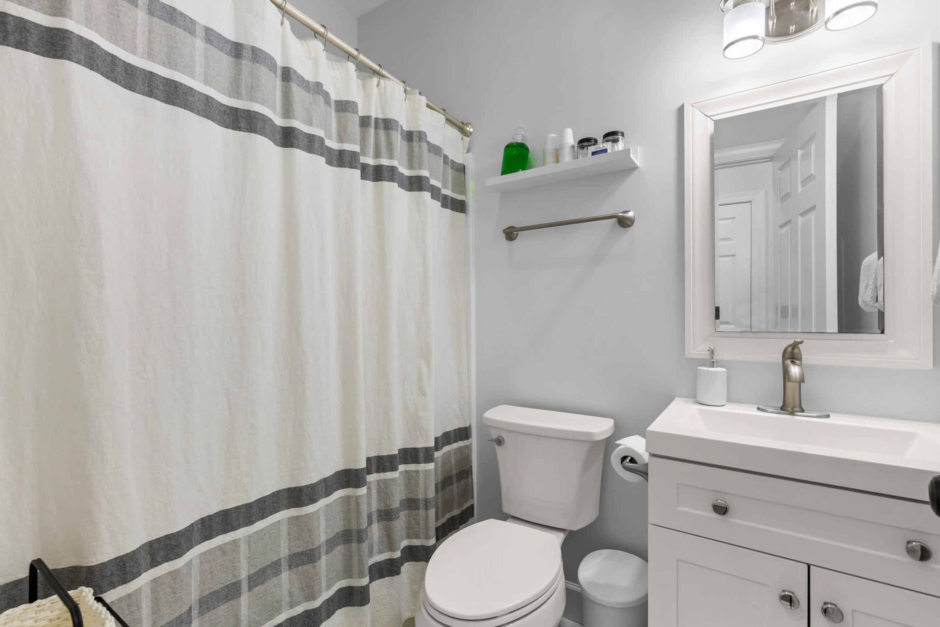 A bathroom with a striped shower curtain, a toilet, a sink with a mirror, and a towel rack.