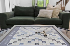 Ein Scrabble-Spiel mit dem Wort 'HOME', platziert auf einem Glastisch vor einem grünen Sofa mit zwei Kissen.