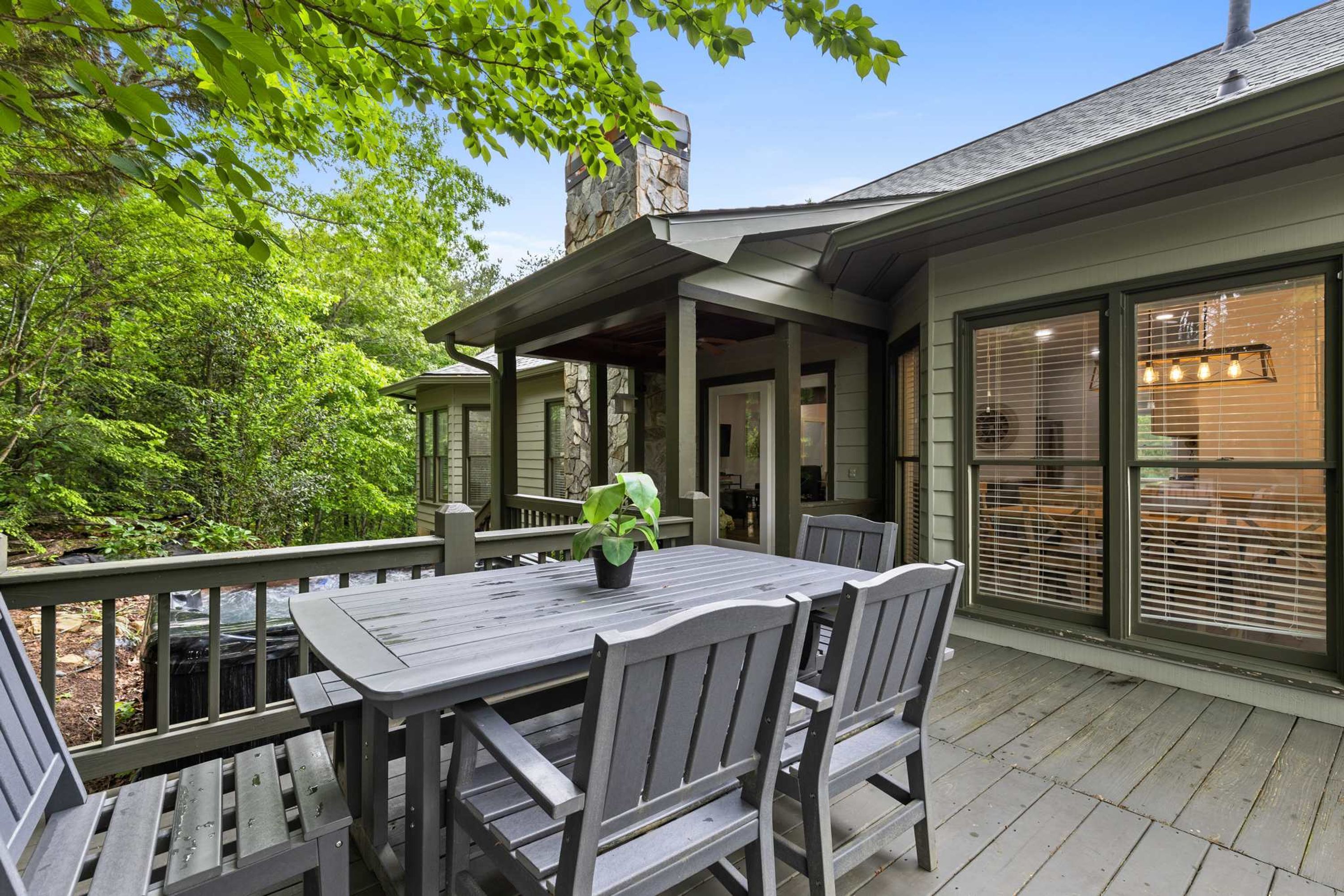 A covered outdoor patio with a table and chairs, surrounded by greenery.