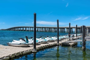 Ein Yachthafen mit dort vertäuten Jetskis, ein klarer blauer Himmel und ein langer Steg, der sich ins Wasser erstreckt.