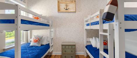 A room with bunk beds, a small dresser, and a window with a view.
