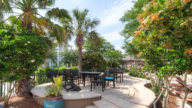 An outdoor patio area with a curved seating arrangement, surrounded by various plants and trees. - Royal Palms Arcade Free Beach Shuttle Pool (Destin)