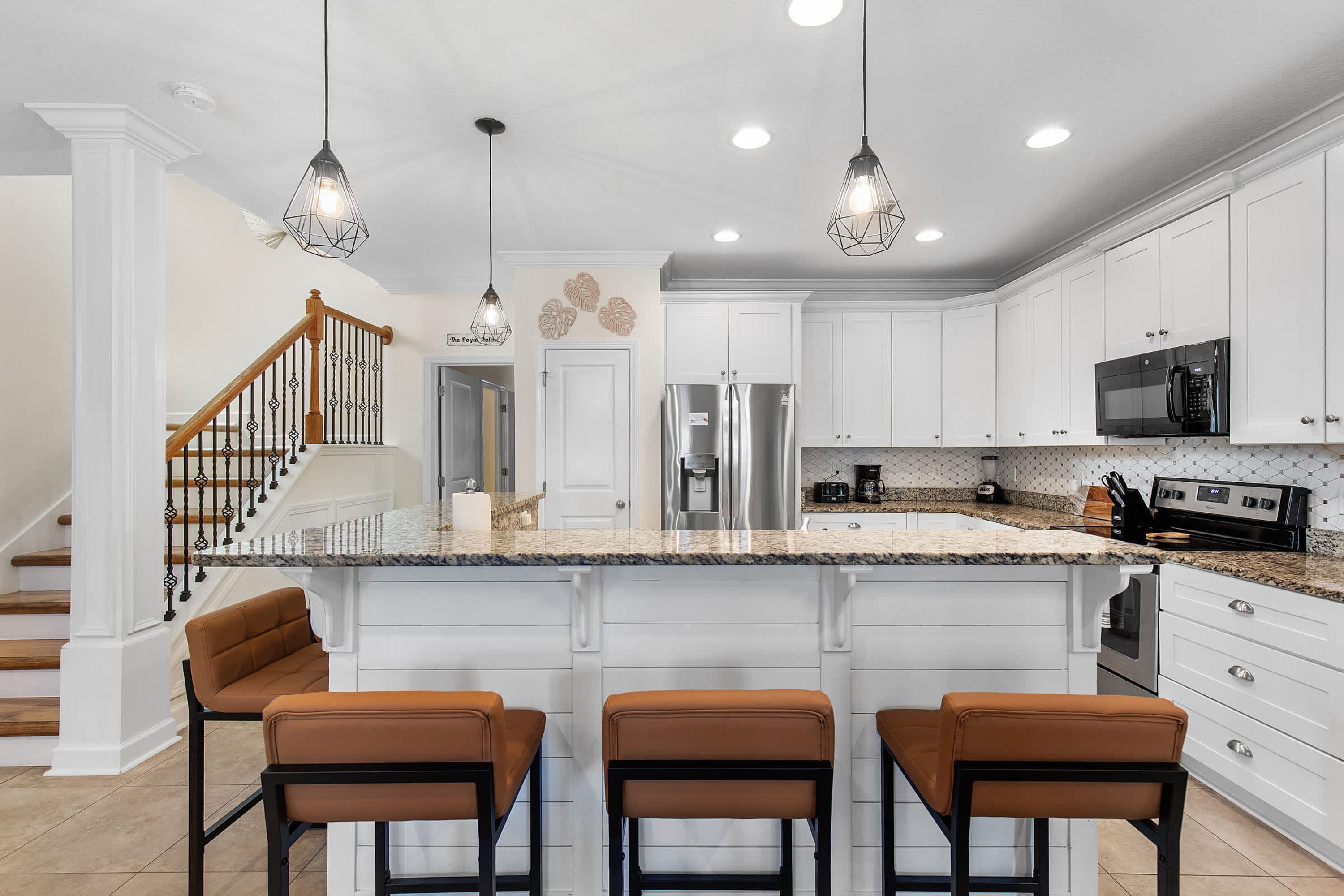 A modern kitchen with white cabinetry, a central island with bar stools, stainless steel appliances, and pendant lighting.