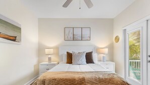 A bedroom with a large bed, two bedside tables with lamps, a ceiling fan, a door with a view, and a painting on the wall. - Royal Palms Arcade Free Beach Shuttle Pool (Destin)