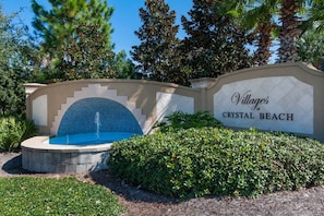 Schild für 'Villages of Crystal Beach' mit einem Brunnen und angelegten Grünflächen.