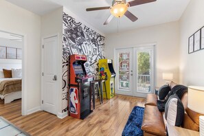 Ein Zimmer mit Deckenventilator, Spielautomaten, einer Couch und einer Tür, die auf einen Balkon führt.