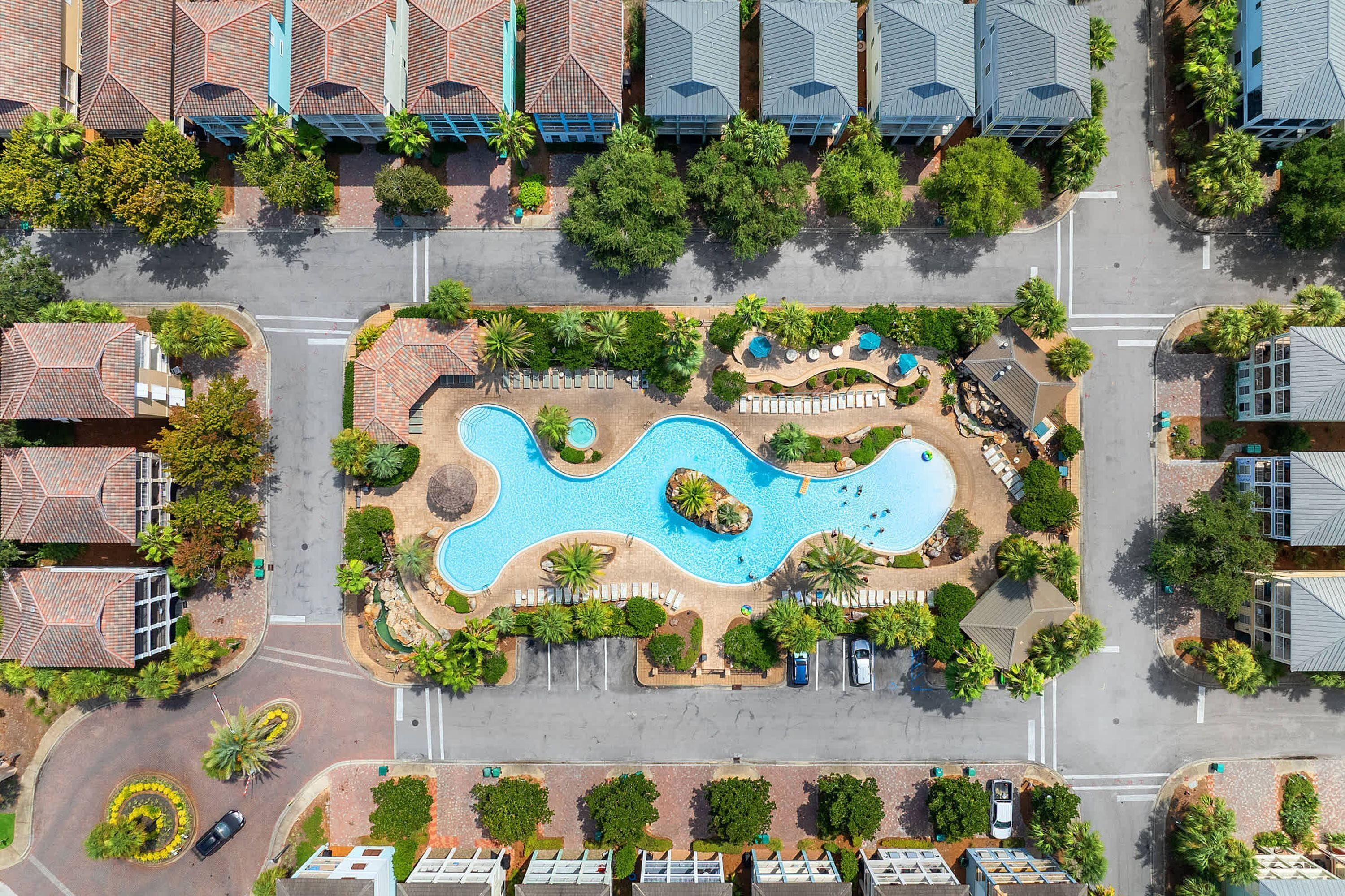 An aerial view of a residential area with a central swimming pool surrounded by greenery and a parking lot.