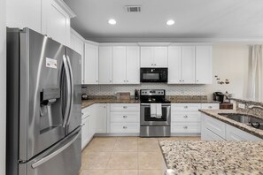 A modern kitchen with white cabinets, stainless steel appliances, a granite countertop, and a built-in oven. - Royal Palms Arcade Free Beach Shuttle Pool (Destin)