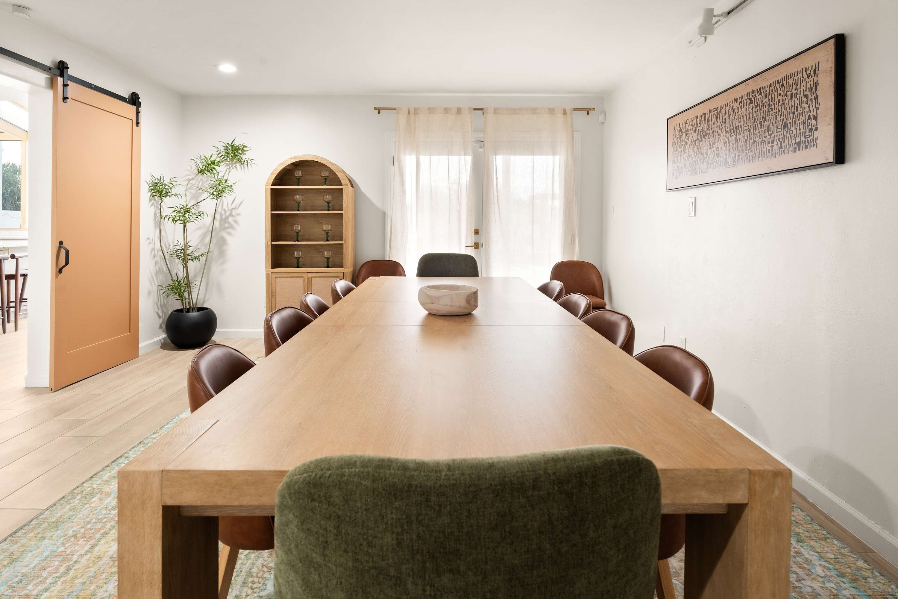 A conference room with a long wooden table, chairs, a bookshelf, and a potted plant.