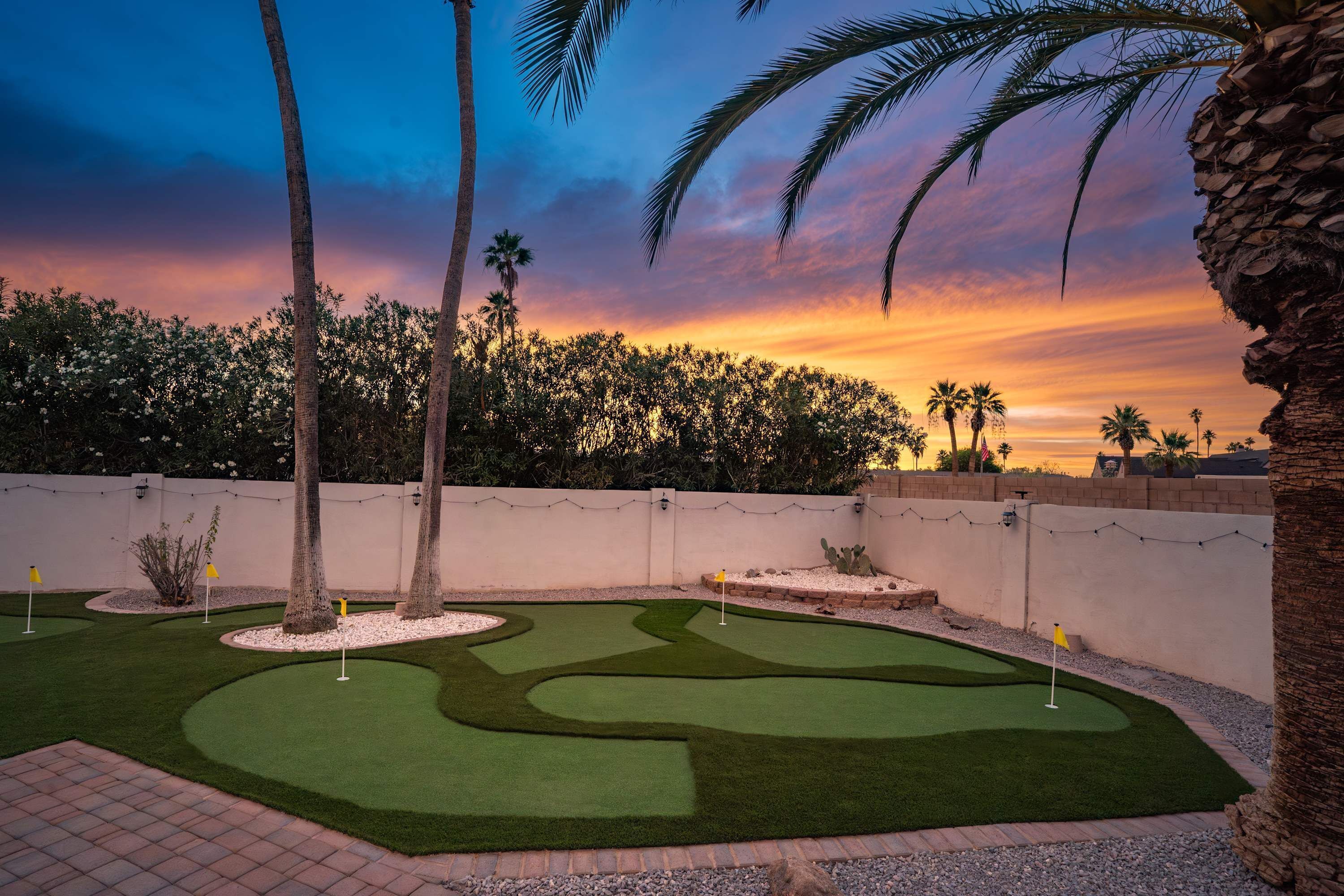 Un campo de golf bien cuidado con un putting green despejado, rodeado de palmeras y un seto.