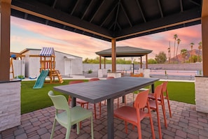 An outdoor patio with a table and chairs, a children's play structure, and a view of a mountain range. - Sonoran Grove Epic Yard With Two Pickleball Courts (Scottsdale)