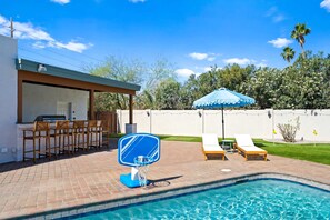 A swimming pool with a blue basketball hoop, lounge chairs, and a barbecue area. - Sonoran Grove Epic Yard With Two Pickleball Courts (Scottsdale)