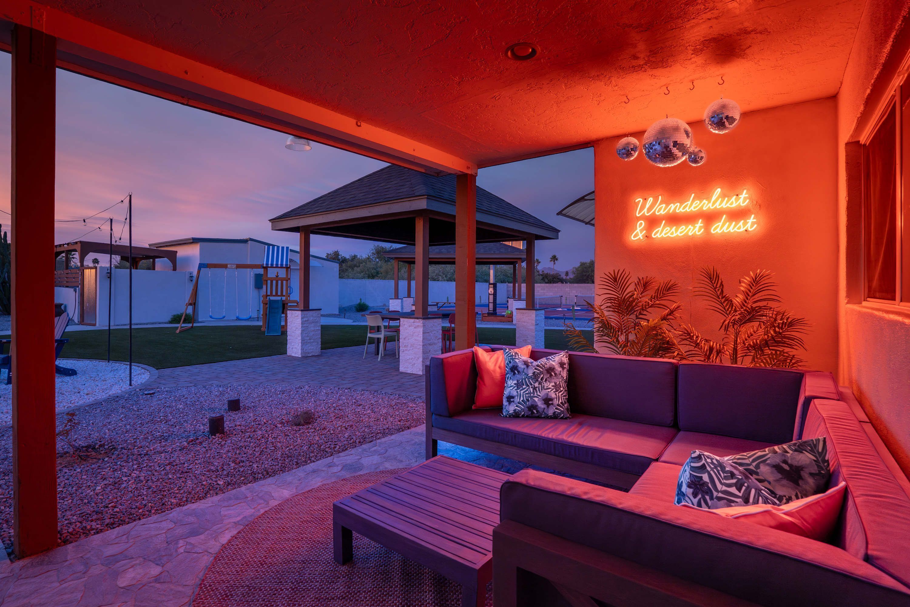 An outdoor seating area with a red neon sign, a covered patio, and a view of the surrounding landscape.