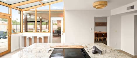 A modern kitchen with a glass enclosure, a built-in stove, and a dining area with a table and chairs.